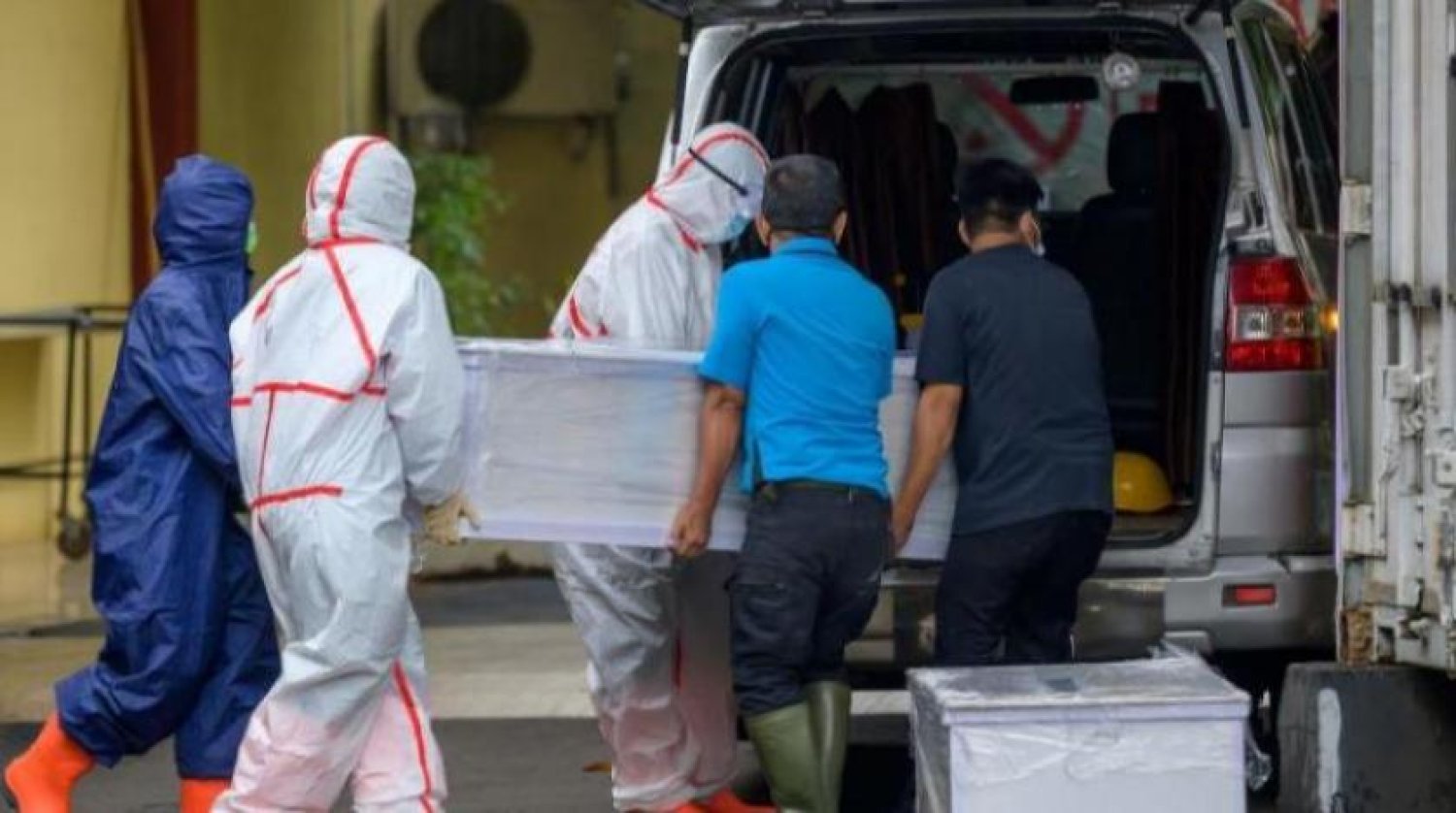 Koruyucu giysiler giyen görevliler bir koronavirüs kurbanının cesedini ambulansa naklediyorlar (AFP)