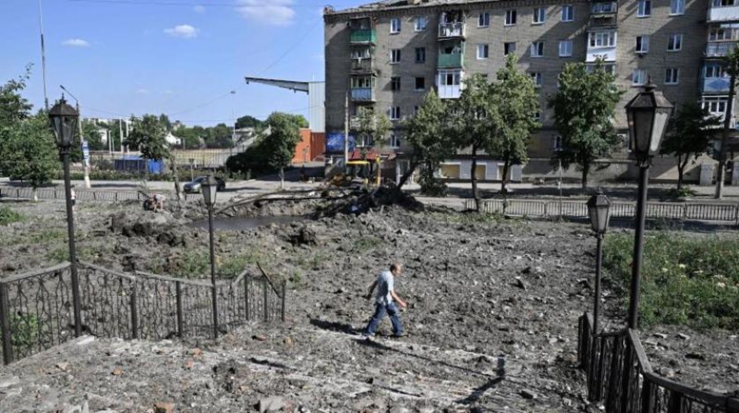 Ukrayna'nın Bakhmut kasabasındaki hasarlı bir apartmanın yakınına roket düşmesi sebebiyle kraterin yanından geçen bir ada (AFP)