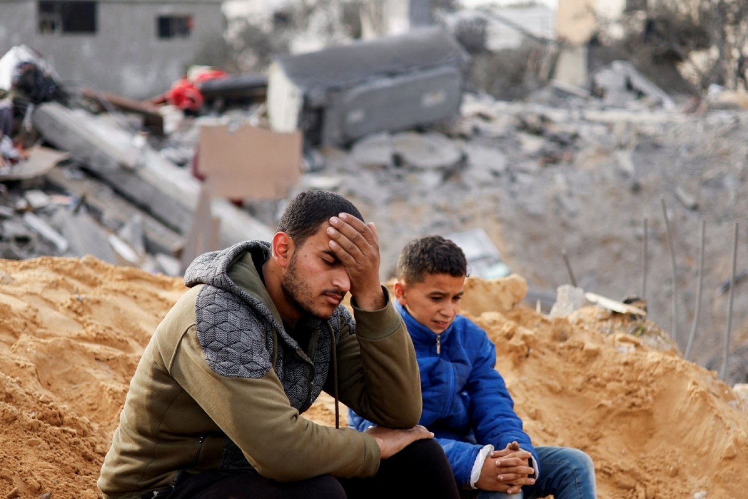 İki Filistinli, 23 Şubat’ta İsrail tarafından Gazze Şeridi’nin güneyindeki Refah’ta bir eve düzenlenen saldırı mahallinde oturuyor (Reuters)