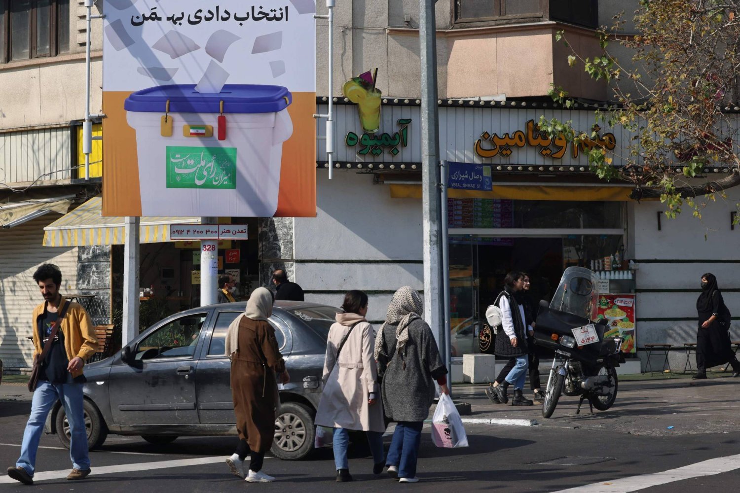  İnsanlar, Tahran’ın merkezindeki bir caddede seçimlere İranlıları katılmaya teşvik eden bir pankartın önünden geçiyor (AFP)