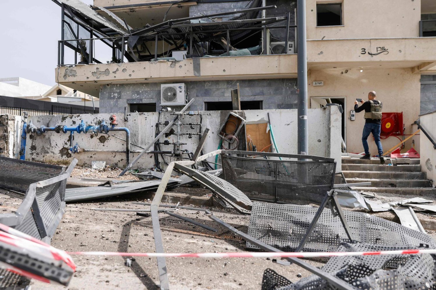 Bir İsrailli, İsrail'in kuzeyinde, Lübnan sınırına yakın Kiryat Shmona'da Hizbullah füzesinin vurduğu bir binayı inceliyor (AFP)