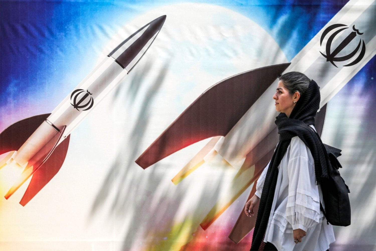 Tahran’ın merkezinde, üzerinde İran İslam Cumhuriyeti’nin armasının olduğu ateşlenmiş bir roketin gösterildiği bir posterin önünden geçen İranlı bir kadın, 15 Nisan 2024 (AFP)