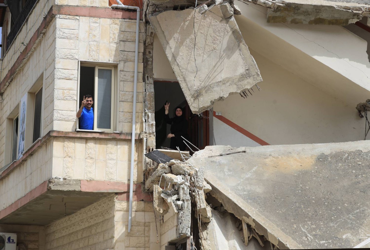 Lübnan'ın güneyindeki Kafr Kila kasabasında İsrail hava saldırısında vurulan evlerinin camından zafer işareti yapan Lübnanlılar (AP)