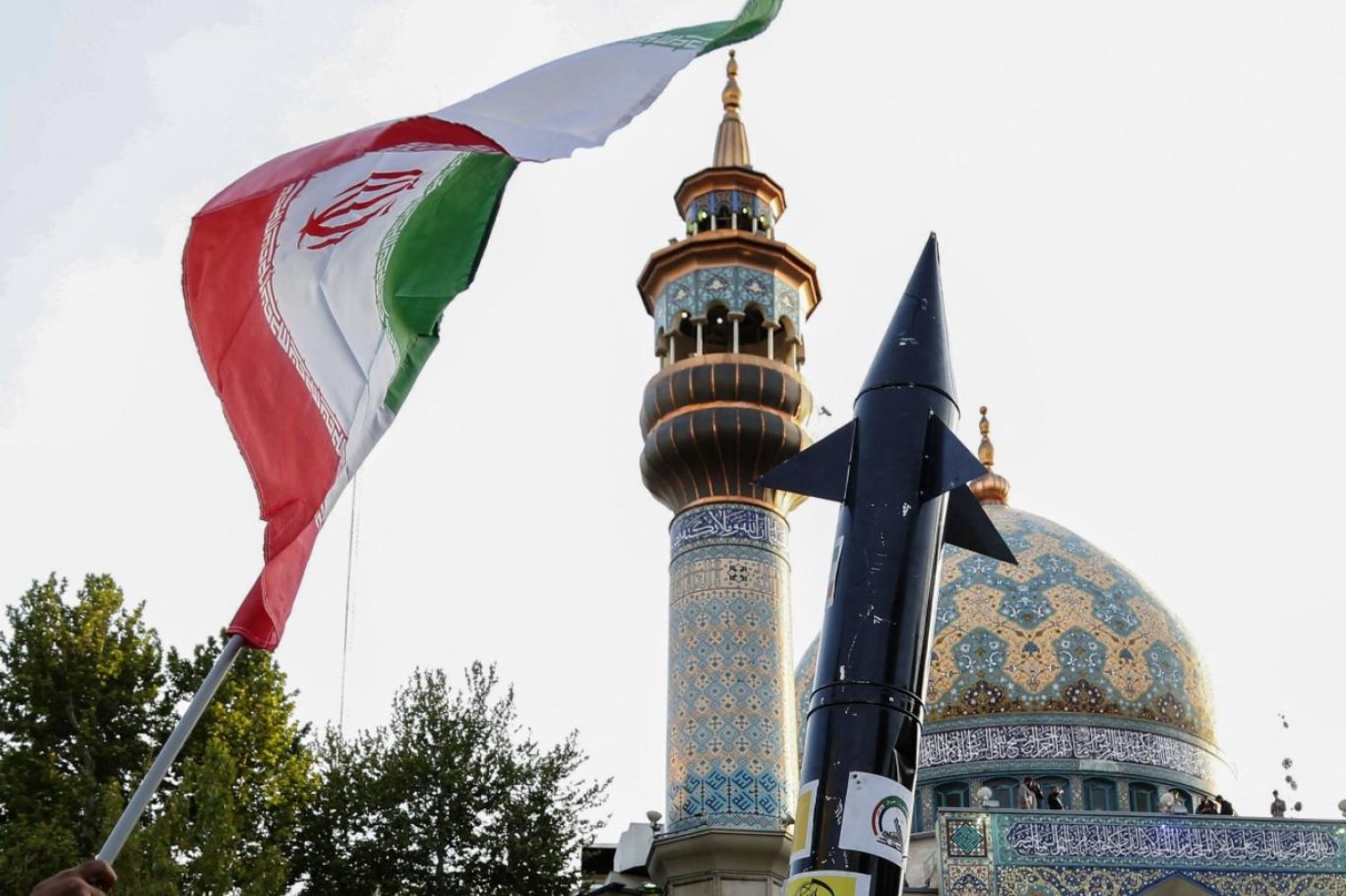 İran'ın İsrail'e saldırısını kutlarken bir elinde İran bayrağı diğer elinde maket bir füze tutan bir İranlı (AFP)