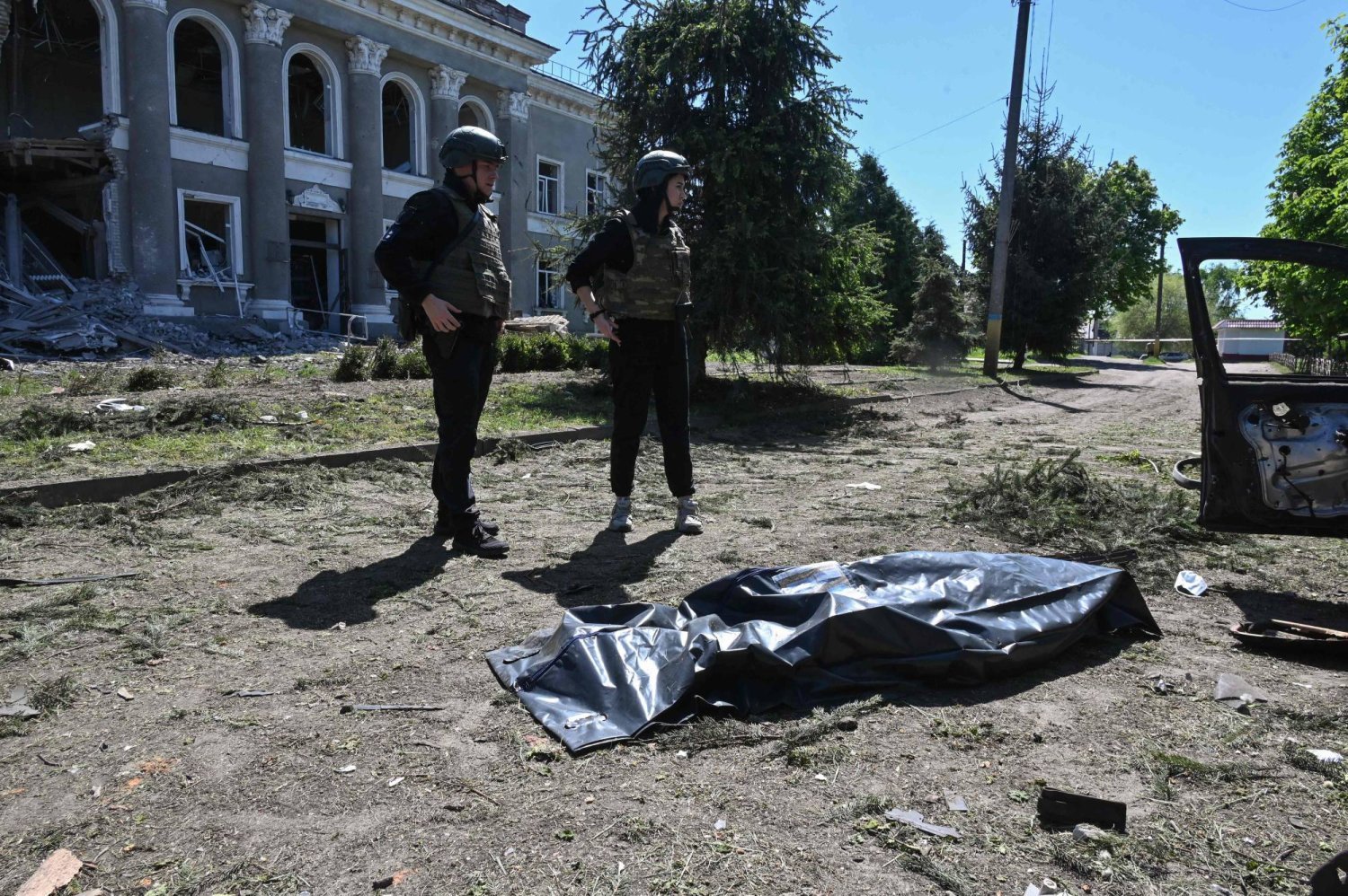 Ukraynalı subaylar, Harkiv bölgesindeki bir köyü hedef alan saldırı sonrası bir cesedin yanında (AFP)