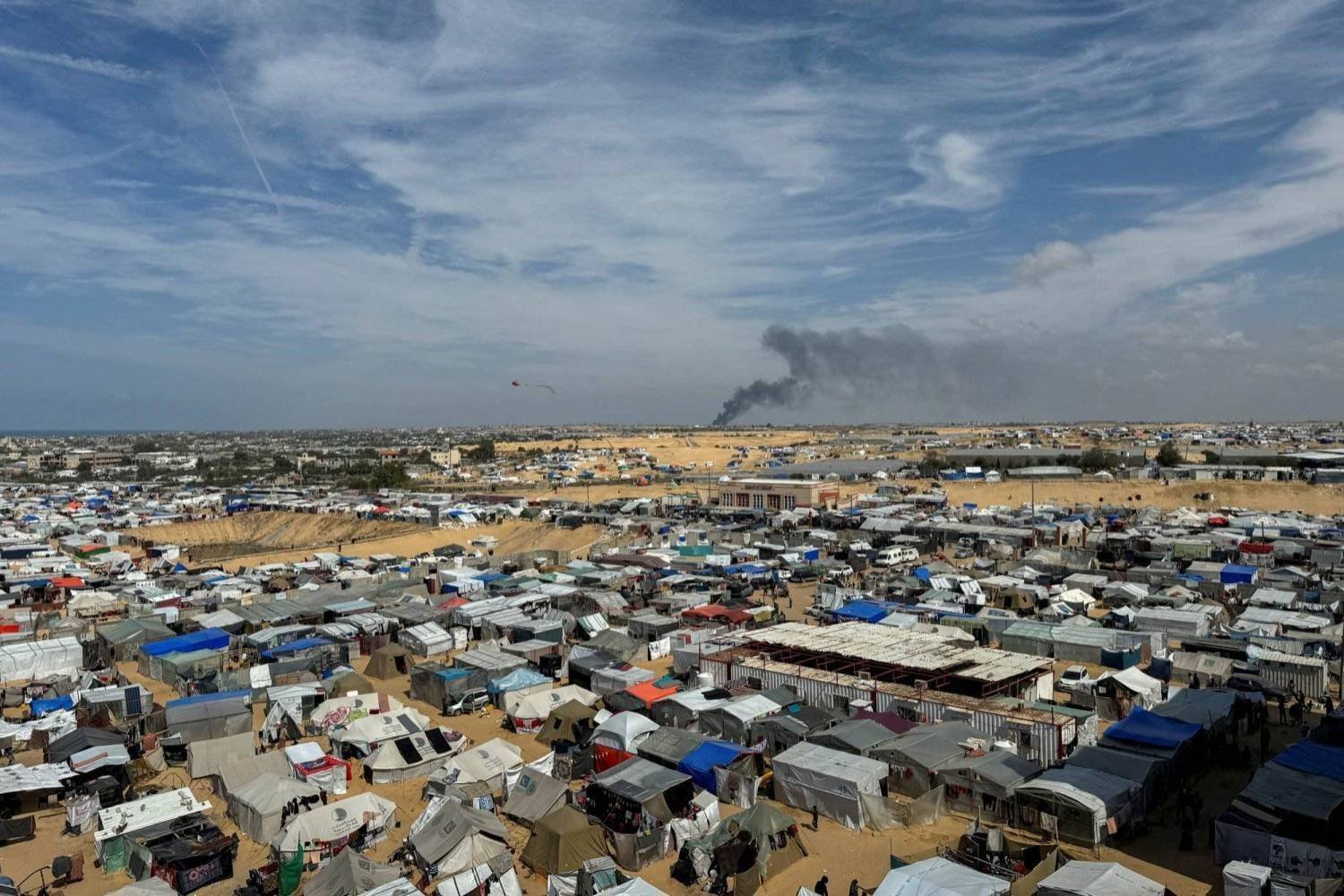 Refah'ta yerinden edilenlerin bulunduğu bir kamp ve arka planda ​​Han Yunus’tan yükselen dumanlar (Reuters)