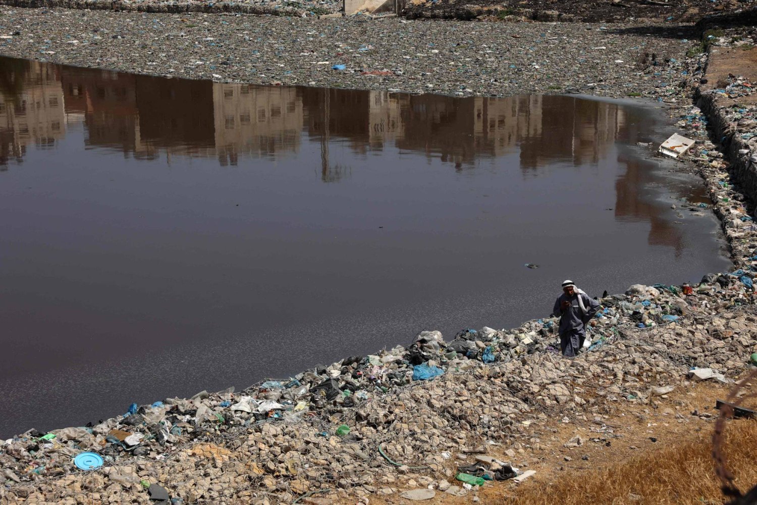 Gazze'de su birikintisinin kenarında çöplerin arasında yürüyen Filistinli (AFP)