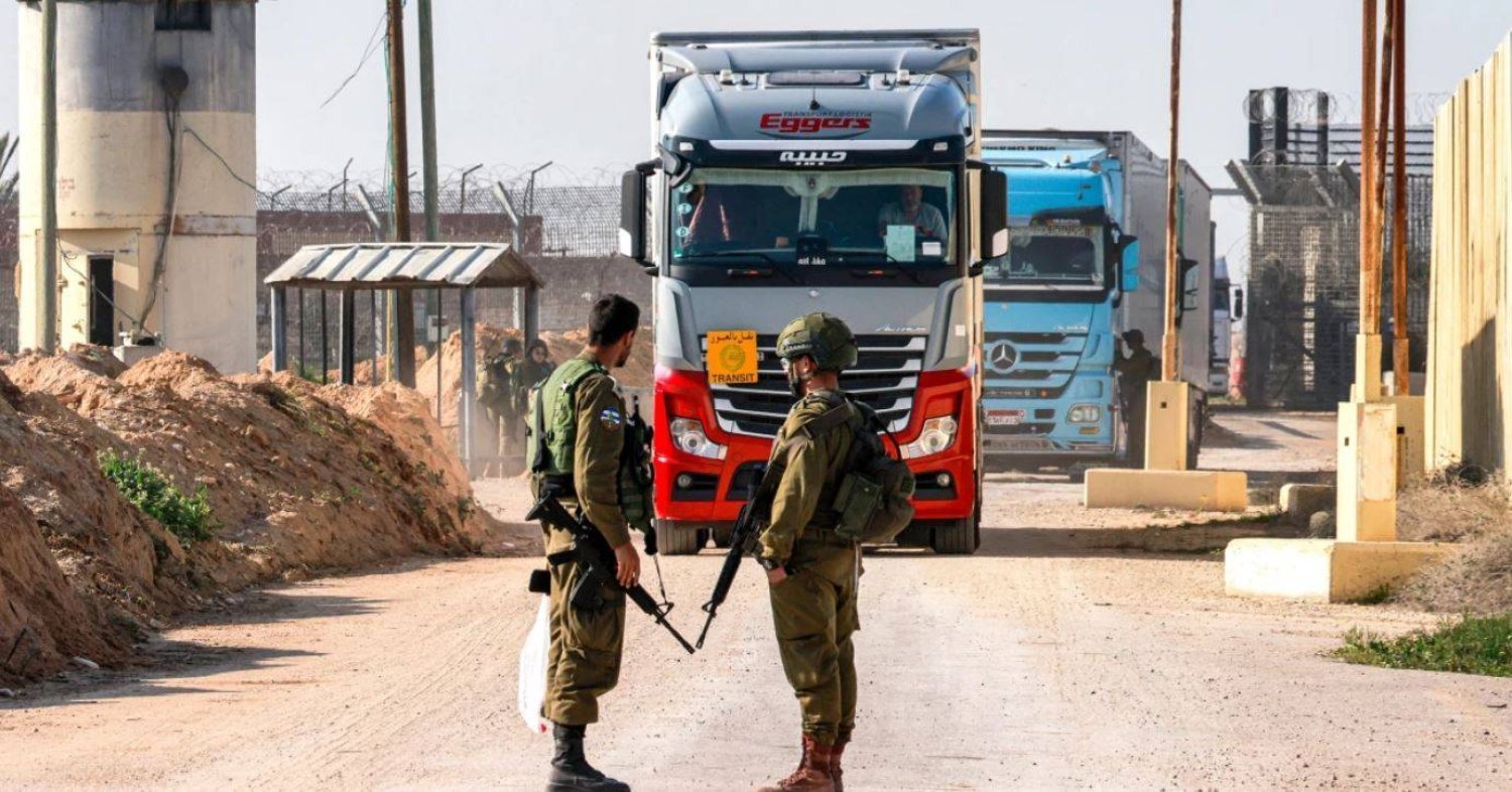 Salı günü, güney Gazze Şeridi ile Kerem Şalom sınır kapısının İsrail tarafında insani yardım yüklü kamyonlar hareket ederken İsrail askerleri nöbet tutuyor (AFP)